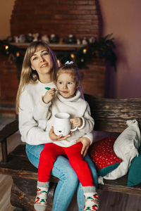 Portrait of a happy little girl sitting on her mother's lap and drinking hot chocolate on christmas