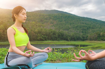 Young woman practicing yoga with friend on exercise mat against mountain