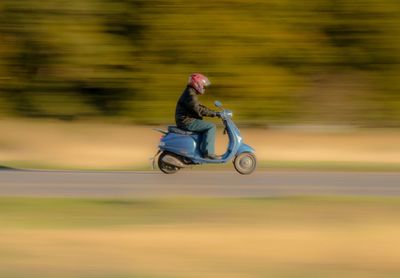 Side view of man riding motor scooter on road