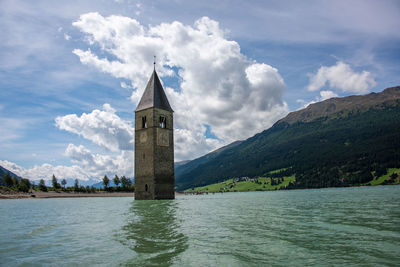 Tower of building by lake against sky