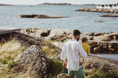 Rear view of father with daughter walking on rock formation by sea