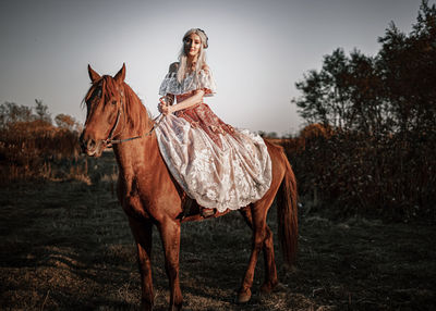 Woman riding horse standing on field