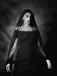 Woman covered with black veil against black background