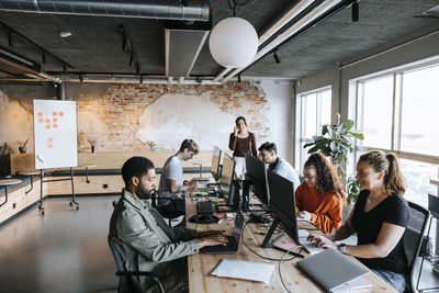 Group of male and female business professionals working on computers at desk in coworking office