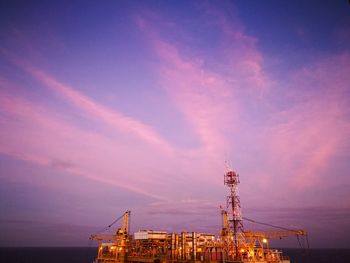 Illuminated offshore platform against sky at sunset