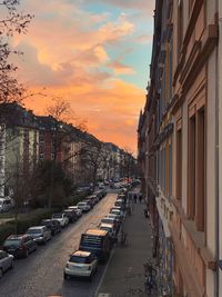 Cars on street amidst buildings against sky during sunset