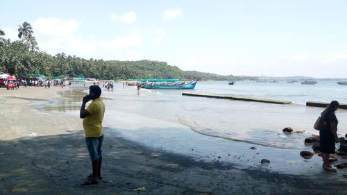 Rear view of people standing on beach against sky