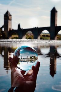 Cropped image of hand holding crystal ball against river in city