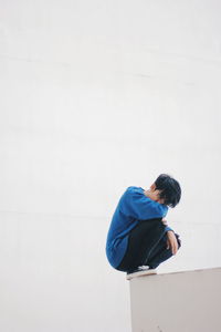 Portrait of man crouching on edge against wall