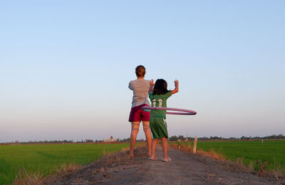 Rear view of girl by mother playing with plastic hoop amidst landscape