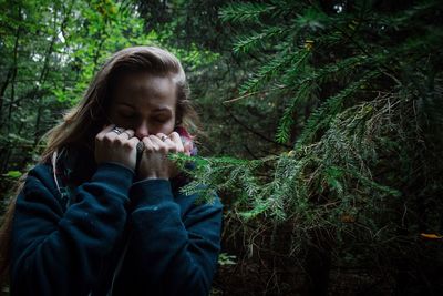 Young woman with eyes closed standing by pine tree in forest