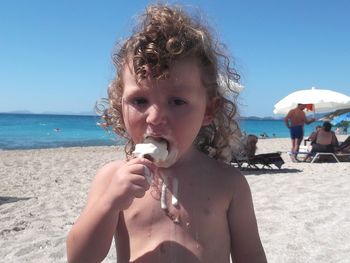 Portrait of shirtless boy on beach against clear sky