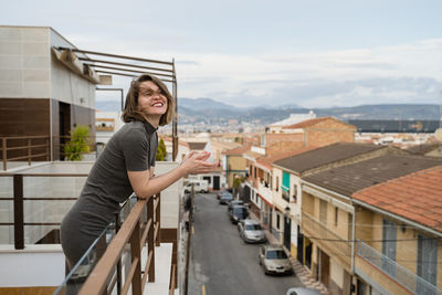 Woman standing by railing in city against sky