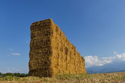 Low angle view of hay bales on field against blue sky