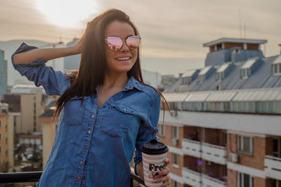 Portrait of young woman having coffee at balcony in city