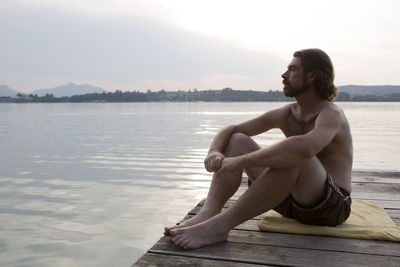 Young man with trunks sitting at a bridge in evening light