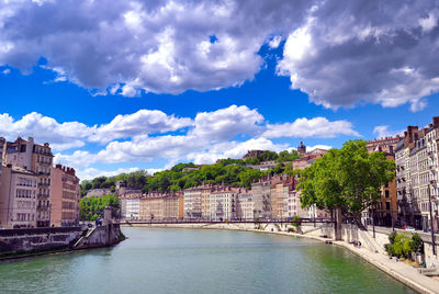 View of buildings by river against cloudy sky