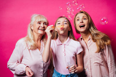 Cheerful family blowing bubbles against colored background