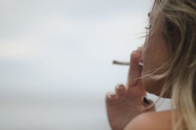 Close-up of young woman smoking cigarette against clear sky