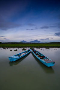 Rowboats moored in river against sky at dusk