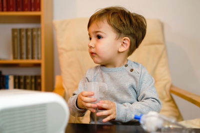 Close-up of cute boy using asthma inhaler at home