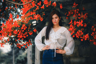 Portrait of beautiful young woman standing against flowering plants