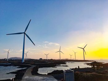 Windmills on beach against sky during sunset