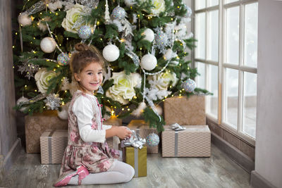 Portrait of smiling girl sitting by christmas tree