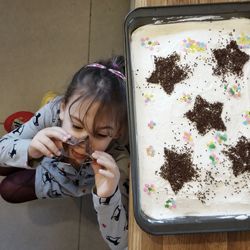 High angle view of playful girl with star shape pastry cutter by birthday cake on table