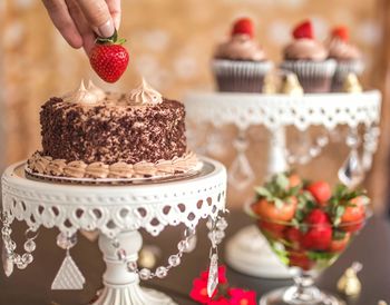 Cropped hand placing strawberry on birthday cake at table
