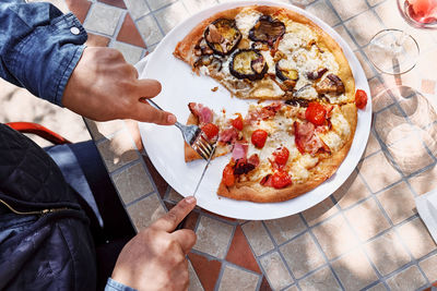 Top view of woman's hands cutting pizza in the plate on the table in the garden. 