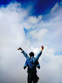 Rear view of man with arms outstretched against sky