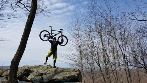 Rear view of man holding bicycle while standing on rock against sky