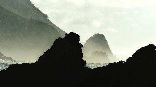 Silhouette rock formations by sea against sky