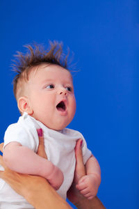 Cute baby boy looking away against blue background