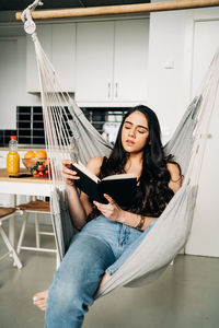 Young woman reading book while resting on hammock