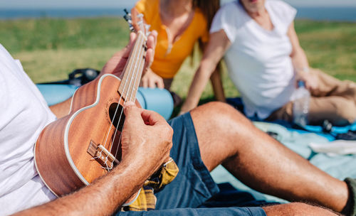 Senior man playing ukulele for his family sitting on a blanket during an excursion
