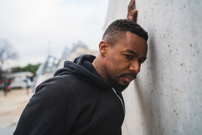 Man looking away while standing against wall