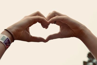 Close-up of hand holding heart shape against sky