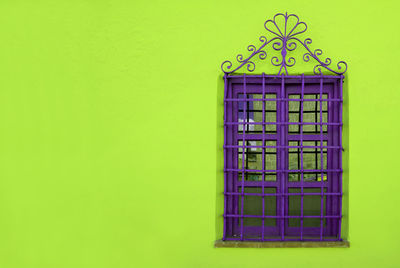 Pop art style vibrant purple wrought iron window on vivid neon green rough concrete wall