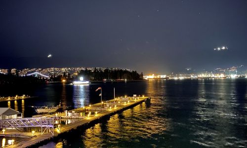 Illuminated pier over river against sky in city at night