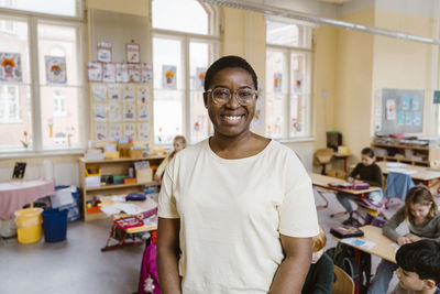 Portrait of smiling teacher standing in front of students at classroom