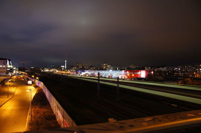 Illuminated railroad tracks in city against sky at night