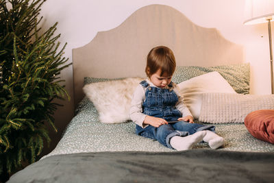 Little child girl on bed with smartphone in christmas cozy atmosphere