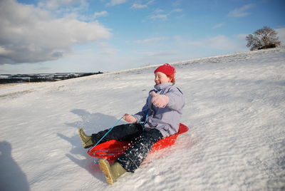 Smiling girl sledging on snow against sky