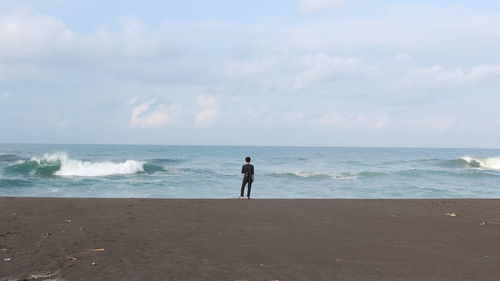 Rear view of man alone standing at beach against sky