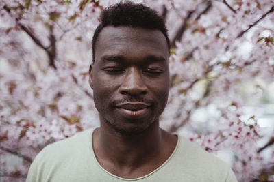 Smiling man with eyes closed standing against tree