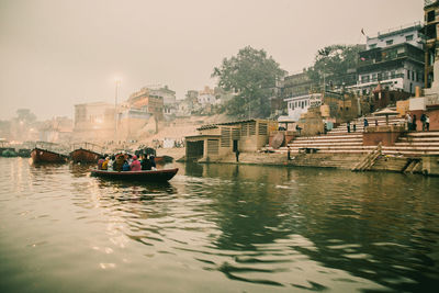 Boats in river by buildings in city against sky