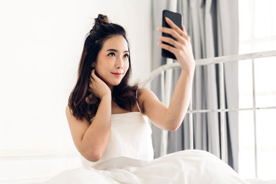 Portrait of young woman using smart phone on bed