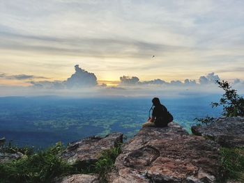 Man sitting on rock against sky